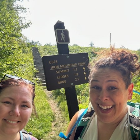 Two hikers cheesing in front of the trailhead sign